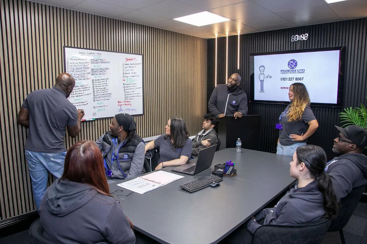PUCIC team members discussing plans around a table and whiteboard